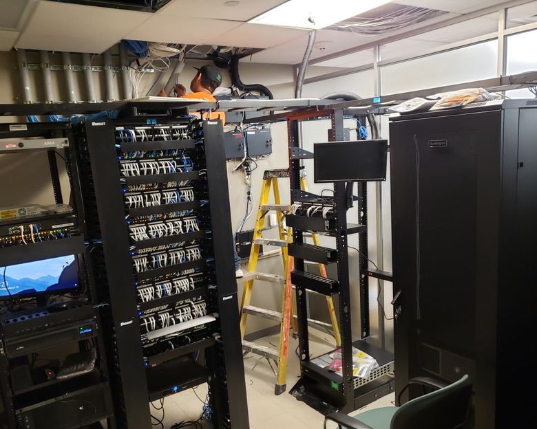 A row of open equipment racks in a server room with overhead cable tray and structured cabling